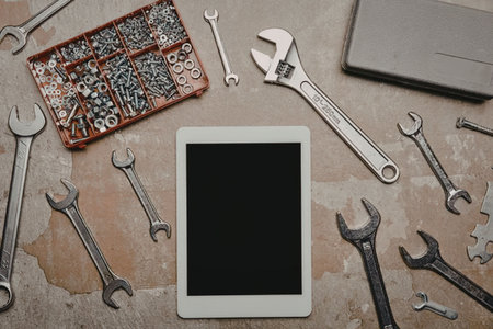 A tablet surrounded by various wrenches and tools on a workbench