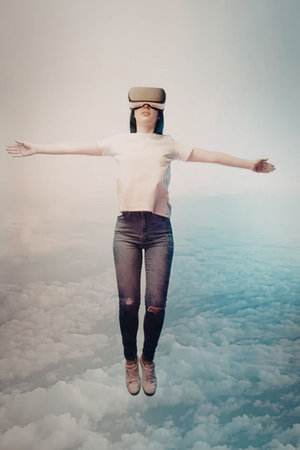 A woman wearing a VR headset floats above the clouds with arms outstretched.の写真素材