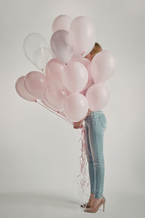 A woman in jeans and heels holding a large bunch of pink balloonsの写真素材