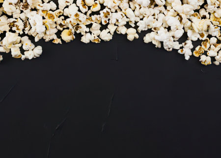 a large pile of white and lightly browned popcorn kernels scattered across the top of a solid black background with a white border at the bottom
