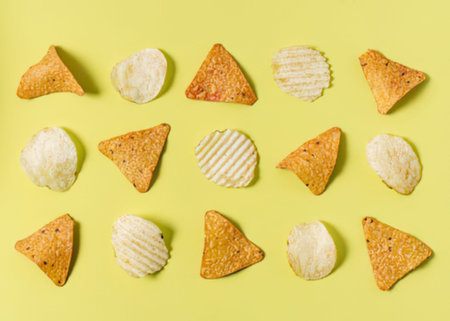an arrangement of potato chips on a pale yellow background, including triangular and round shapes, with some having ridged surfaces