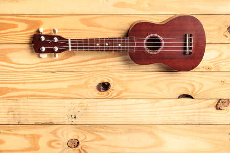 brown ukulele rests on a wooden floor. Use as Wallpaper