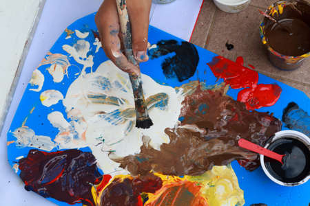 The painter uses red, blue, yellow, black and white to mix colors to paint.の写真素材