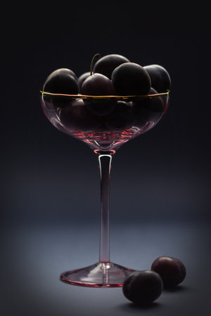Still life - plums in a glass goblet Beautiful purple plums in a glass goblet. still life. Decoration. Dessert. dark background.の写真素材