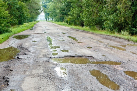 Potholes on the road with stones on the asphalt. The asphalt surface is destroyed on the road. Bad condition of the road, needs repair. Construction and repair of roads.の写真素材