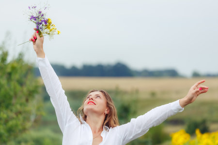 Gentle beautiful young woman enjoying the sun, holding a bouquet of wildflowers. A charming girl with a bouquet of wild flowers. Summer tender photo.の写真素材