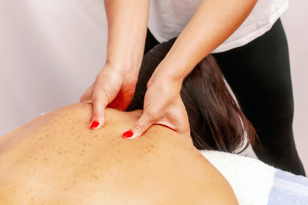 relaxed young woman lying face down on massage table enjoying therapeutic body massage by professional masseur in spa or wellness center.の写真素材