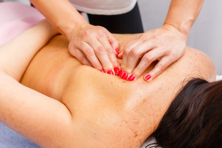 relaxed young woman lying face down on massage table enjoying therapeutic body massage by professional masseur in spa or wellness center.の写真素材