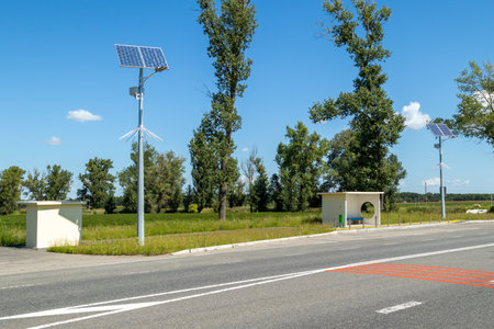 Lamp post with solar panel system on road with blue sky and trees. Autonomous street lighting using solar panels. Street lamp, on batteries from the sun. Alternative renewable energy systems.の写真素材