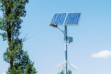 Solar device with street lamp on background of blue sky. Street light powered by solar panel with battery included. Alternative energy from the sun.の写真素材