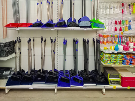 Various brooms, dustpans, and household cleaning supplies neatly arranged on shelves in a retail store for home maintenance.の写真素材