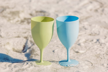 Two bright, pastel-colored plastic wine glasses stand in a row on a surface, creating a bright contrast with the white background.の写真素材