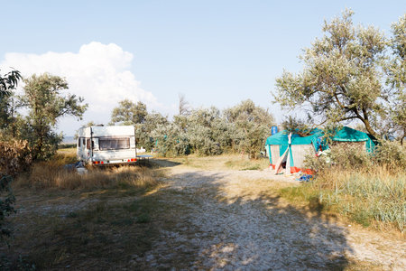 A peaceful outdoor campsite featuring a caravan and a large tent set up in a rural area with trees, grass, and open sky.の写真素材