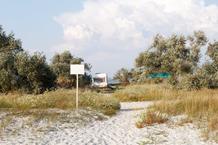 A caravan is parked near a sandy beach, surrounded by wild vegetation and trees, creating a peaceful and secluded camping spot.の写真素材