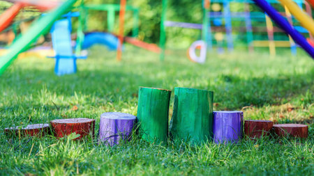 Vibrantly painted wooden stumps arranged on green grass in an outdoor playground with colorful equipment in the background.の写真素材