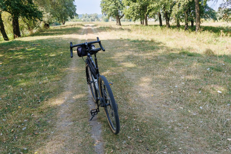 The bike sits on a dirt track in the quiet countryside, surrounded by trees and grassy fields, perfect for quiet outdoor adventures or bike tours.の写真素材