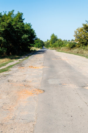 Bad road, cracked asphalt with potholes and big holes. The asphalt surface is destroyed on the road. Bad condition of the road, needs repairの写真素材