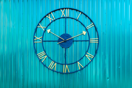 A decorative outdoor clock with Roman numerals and gold hands mounted on a bright blue corrugated metal wall, showing the time.の写真素材