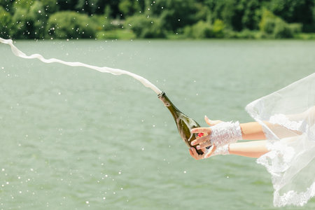 the bride opens a bottle of champagne with splashes. Close-up.の写真素材