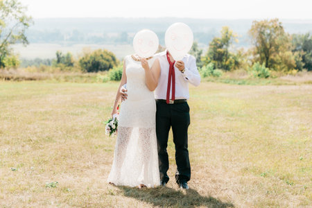 Newlyweds with white balls. Funny photo with newlyweds. The newlyweds covered their faces with white balls with a happy emoticon. Two people are holding white balloons with emoticons painted on them.の写真素材