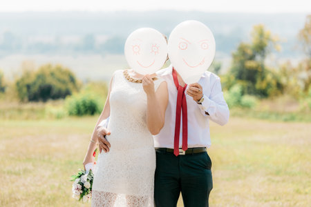 Newlyweds with white balls. Funny photo with newlyweds. The newlyweds covered their faces with white balls with a happy emoticon. Two people are holding white balloons with emoticons painted on them.の写真素材