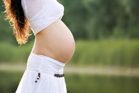 Close-up of a pregnant woman's belly on a green natural background. Concept of healthy pregnancy, expectant motherの写真素材