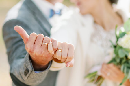 A romantic close-up of a bride and groom linking pinky fingers, showing their wedding rings in soft natural light.の写真素材