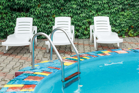 Outdoor pool with steps and railings at the resort. Pool with steps and water. Stainless steel stairs for descent into the pool. Three white sunbeds are located near a round pool with blue water.の写真素材