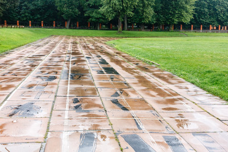 Old damaged running track in stadium with faded white lines and broken tiles, surrounded by green grass and fields. Urban sports facilities concept.の写真素材