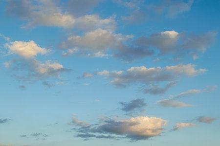 Soft, scattered clouds float across a blue sky during dusk, creating a serene and peaceful atmosphere with warm light reflections.の写真素材