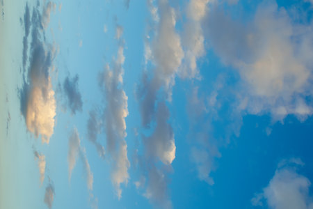 Soft, scattered clouds float across a blue sky during dusk, creating a serene and peaceful atmosphere with warm light reflections.の写真素材