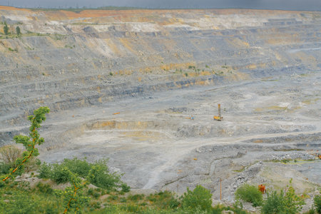 A open-pit mine with visible excavation sites, dirt roads, and industrial equipment, surrounded by sparse vegetation and rocky terrain.の写真素材