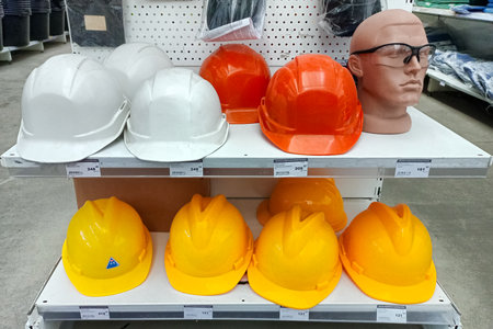 A variety of construction safety helmets in white, orange, and yellow displayed on store shelves,...