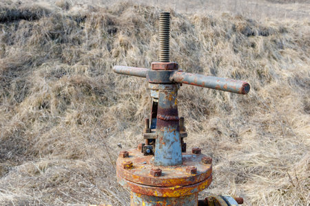 A weathered and rusty yellow gas pipeline valve stands in a dry grassy field, showing signs of aging, corrosion, and neglect.の写真素材