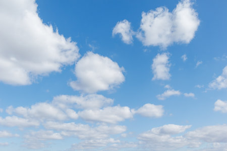 Bright blue sky with fluffy white clouds scattered across, creating a peaceful and refreshing atmosphere on a sunny day.の写真素材