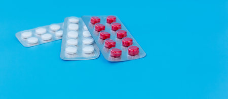 Assorted blister packs with red and white tablets placed on a bright blue background, symbolizing medication, healthcare, and treatment.の写真素材