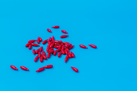 Top view of multiple red capsules spread across a vibrant blue surface, ideal for health, supplement, or pharmaceutical themes.の写真素材