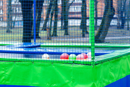 Trampoline surrounded by safety net, set in an outdoor play area, with various colorful balls scattered on its surface, highlighting recreational play activities for childrenの写真素材