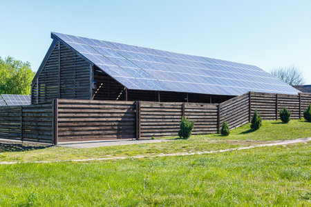 Large array of solar panels set up in a fenced area under clear blue sky, surrounded by greenery and small bushes.の写真素材