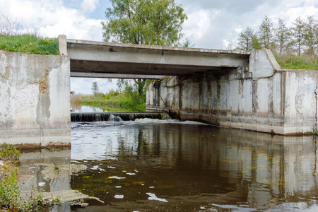 A reinforced concrete bridge spans a controlled water channel with a low-head weir, used for flood management and water flow regulation.の写真素材