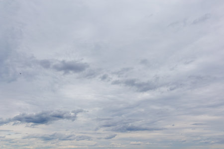 Wide view of a cloudy sky filled with layered gray clouds on an overcast day, showing subtle texture...