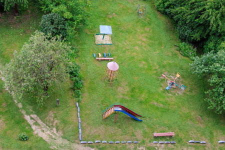 Top-down view of a vintage outdoor playground surrounded by grass and trees, featuring a slide,...