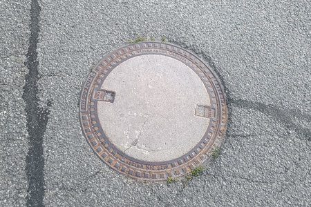 Round concrete manhole cover with metal rim embedded in a cracked asphalt road surface, showing wear and urban decay.の写真素材