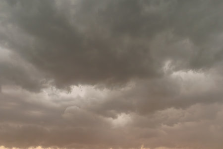Dramatic view of dark storm clouds gathering in the sky with faint golden light peeking through the...