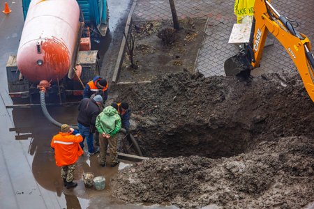 Ukraine, Romny, December 24, 2024: road construction workers repairing underground utilities with an...