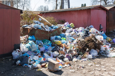 Large pile of household garbage and plastic waste overflowing from a dumpster near residential...