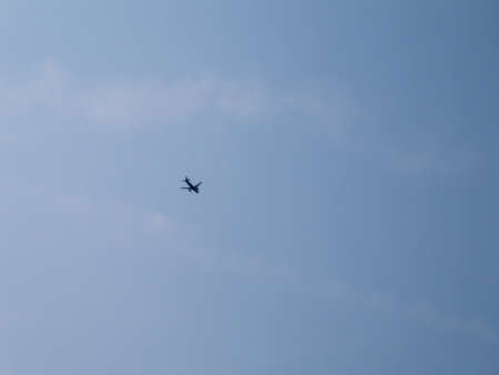 Silhouette of high flying plane, flying from left to right, under blue sky at day.