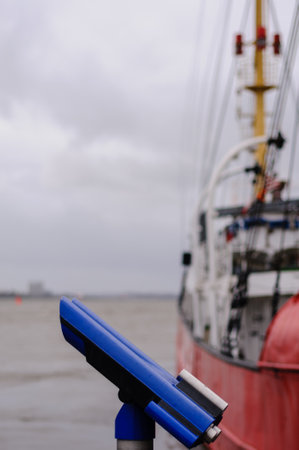 Hamburg, Germany - March 13, 2014: Telescope at the pier of the museum haven Oevelgoenne with light vessel Elbe 3 in blurry background.のeditorial素材