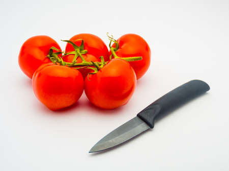 Fresh red tomatoes and a black ceramic knife isolated on white background.の写真素材