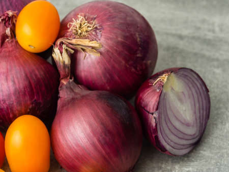 Close-up of group of red onions and two small yellow snack tomatoes. One onion sliced. Selective focusの写真素材